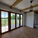 salon z panelami drewnianymi, białymi ścianami i oknami tarasowymi, wykończony przez firmę budowlaną MM Bujak